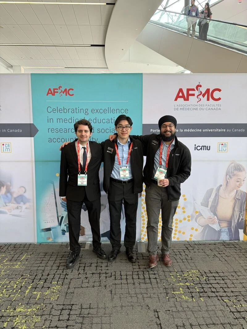 Three conference attendees standing together in front of the AFMC and ICAM 2026 backdrop.